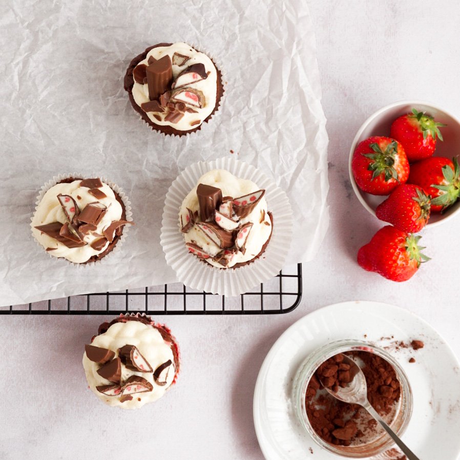 Dieses Bild zeigt vier Yogurette Muffins mit Yogurette Frostingvon oben,, sowie ein Schälchen mit Erdbeeren und eins mit Kakaopulver