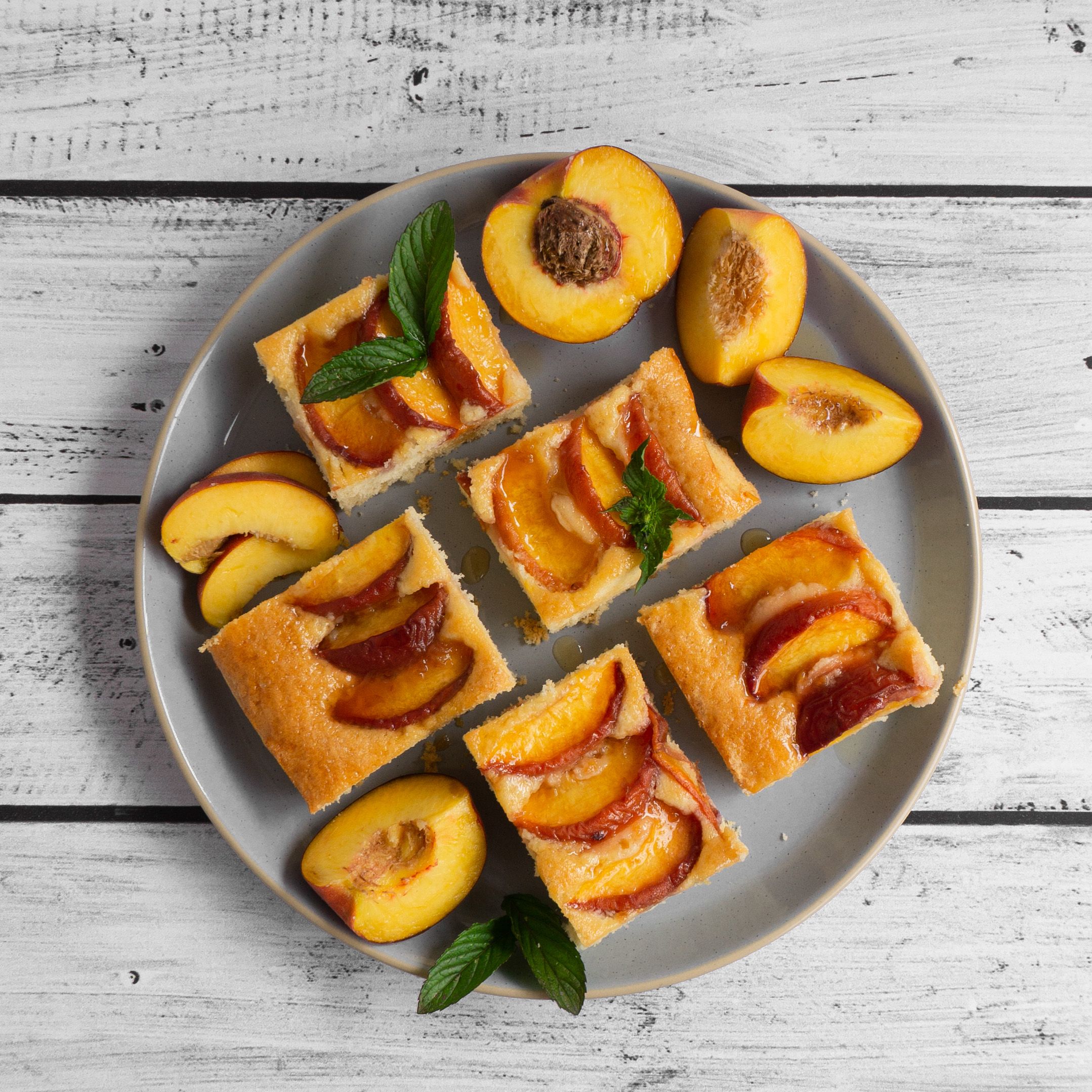 Dieses Bild zeigt fünf Stücke Pfirsichkuchen auf einem Kuchenteller von oben mit frischer Minze und frischen Pfirsichspalten